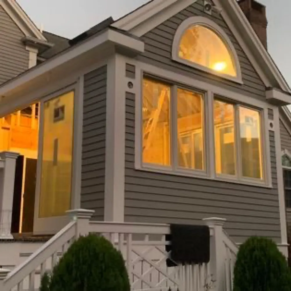 Sunroom addition with gray siding and arched window glowing at dusk